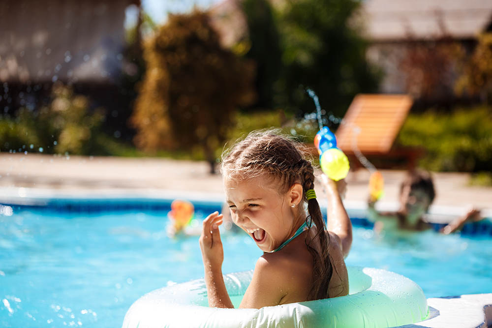 Cheerful children playing waterguns, rejoicing, jumping, swimming in pool. Copy space